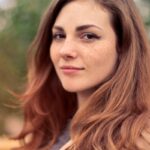 A young woman with long hair smiles confidently for an outdoor portrait session.